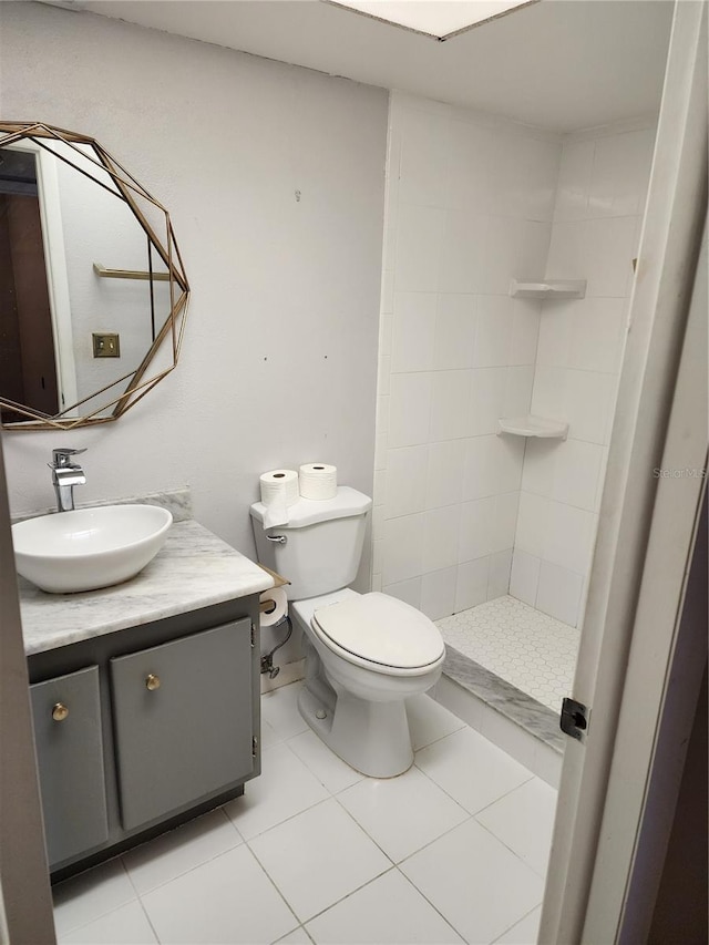 bathroom with toilet, tile patterned flooring, vanity, and tiled shower