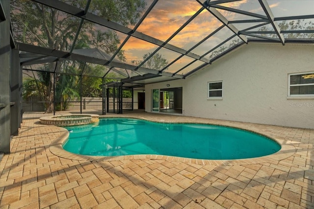 pool at dusk with an in ground hot tub, a patio area, and glass enclosure