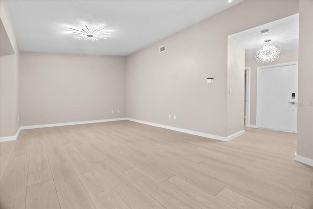 unfurnished room featuring a notable chandelier, a textured ceiling, and light wood-type flooring