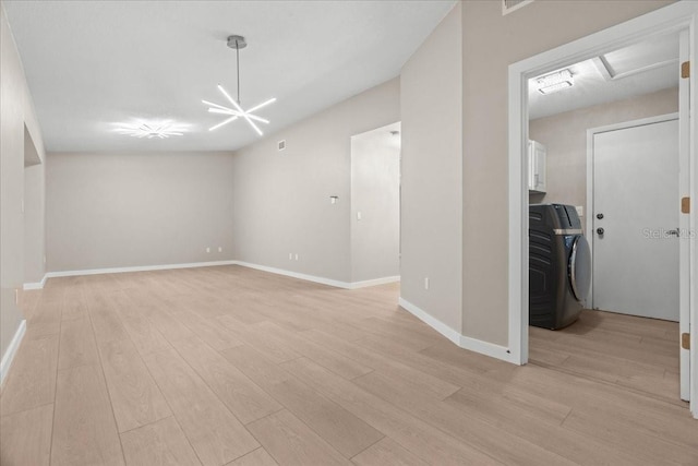 unfurnished room featuring an inviting chandelier, light wood-type flooring, and washer / clothes dryer