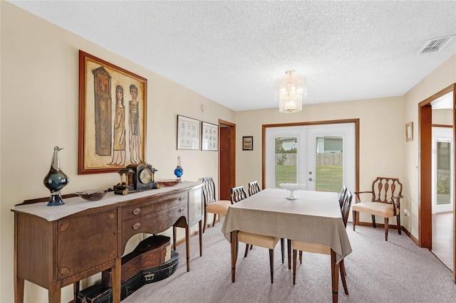 carpeted dining space featuring french doors, a textured ceiling, and a chandelier