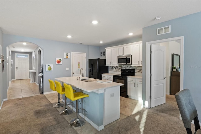 kitchen with a breakfast bar area, an island with sink, light carpet, black appliances, and white cabinets