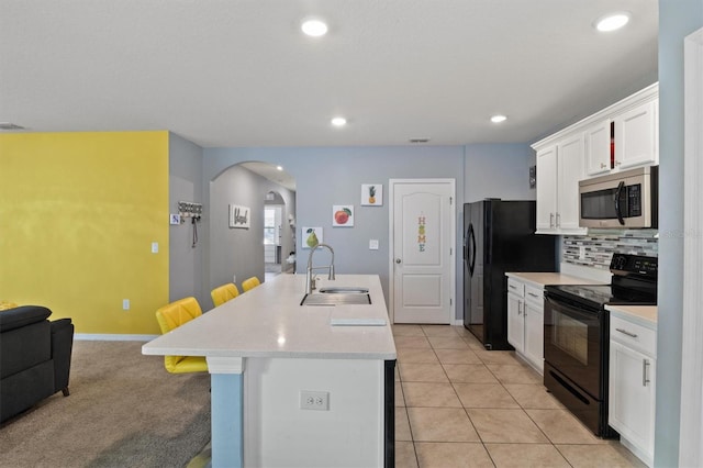 kitchen with white cabinets, light tile patterned floors, a kitchen bar, black appliances, and sink