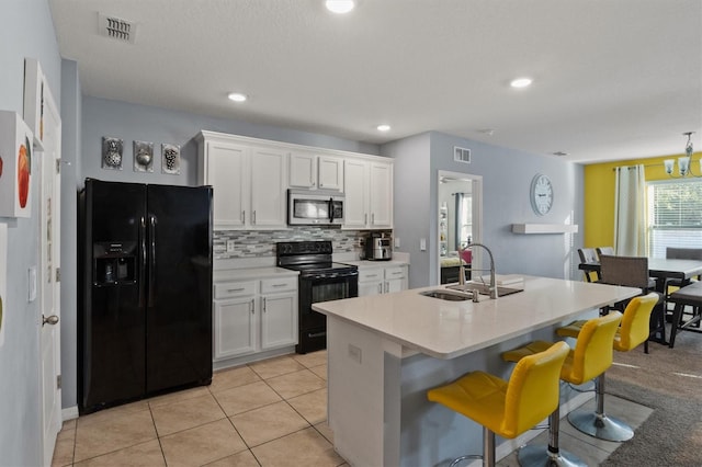 kitchen featuring a kitchen island with sink, sink, black appliances, a kitchen bar, and white cabinetry