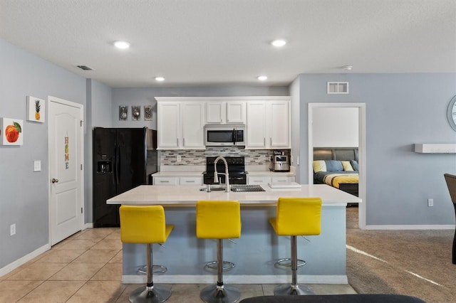 kitchen featuring a center island with sink, black appliances, white cabinetry, and a breakfast bar