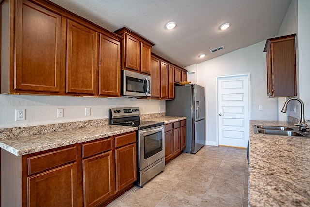 kitchen featuring light stone countertops, lofted ceiling, appliances with stainless steel finishes, and sink