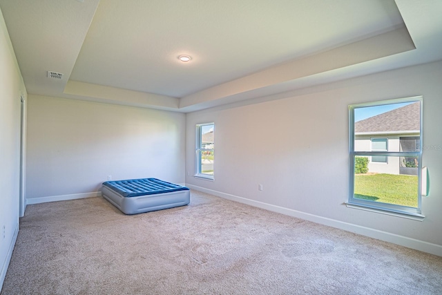 unfurnished bedroom featuring light colored carpet and a tray ceiling