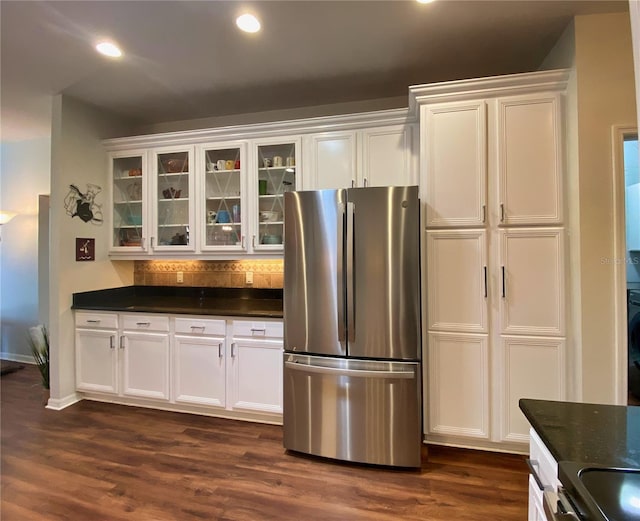 kitchen featuring decorative backsplash, dark hardwood / wood-style floors, dark stone countertops, stainless steel fridge, and white cabinets