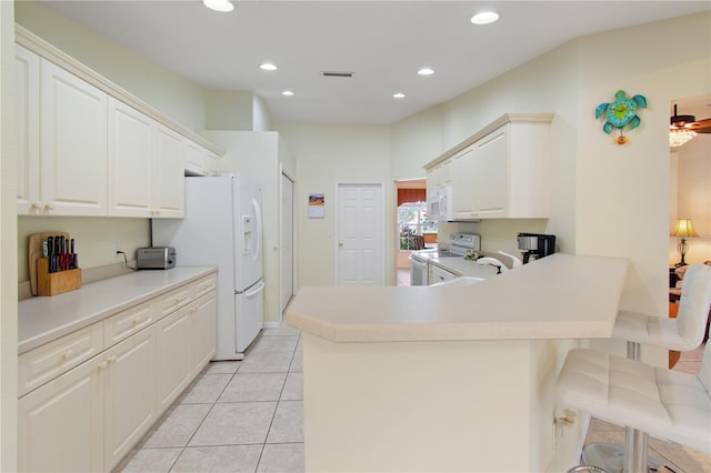 kitchen featuring white appliances, a kitchen bar, kitchen peninsula, and white cabinets