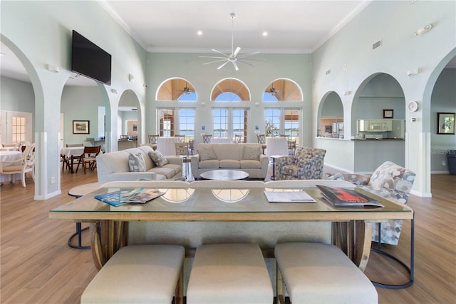 living room with crown molding, a high ceiling, light wood-type flooring, and ceiling fan