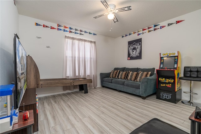 living room with a textured ceiling, light wood-type flooring, and ceiling fan