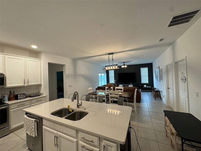 kitchen featuring appliances with stainless steel finishes, sink, white cabinetry, light tile patterned floors, and a kitchen island with sink