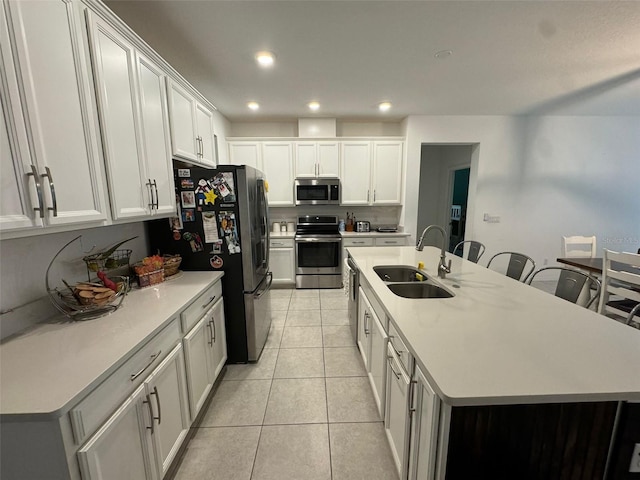 kitchen with appliances with stainless steel finishes, light tile patterned flooring, sink, an island with sink, and white cabinets