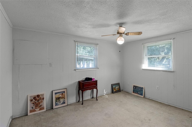 spare room featuring a wealth of natural light, wooden walls, a textured ceiling, and ceiling fan