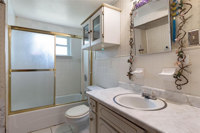 full bathroom with tile patterned floors, toilet, vanity, tile walls, and enclosed tub / shower combo