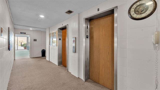 hall featuring elevator, light colored carpet, and a textured ceiling