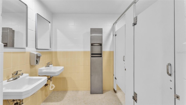 bathroom with tile patterned flooring, dual sinks, and tile walls