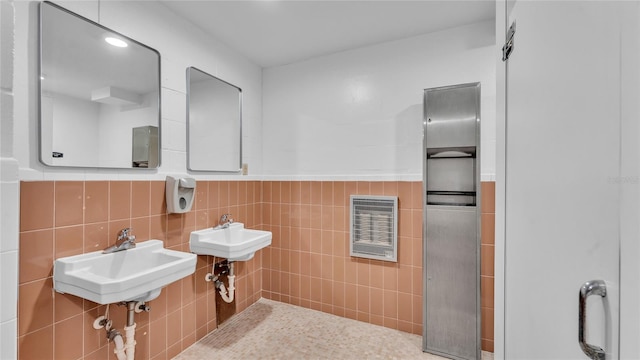 bathroom featuring heating unit, tile walls, and double sink