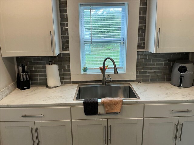 kitchen with white cabinets, light stone counters, sink, and tasteful backsplash