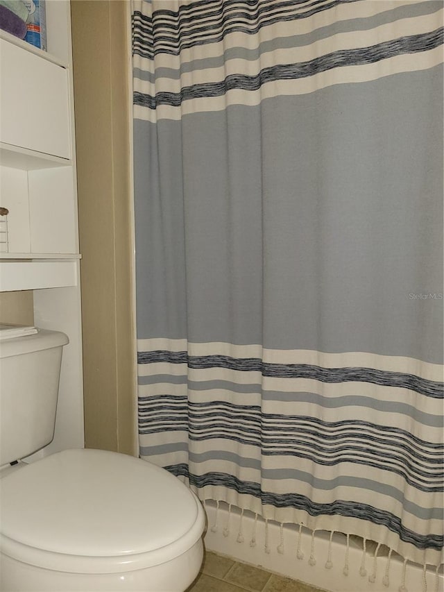 bathroom featuring a shower with shower curtain, toilet, and tile patterned flooring