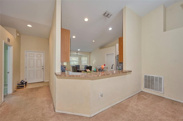 kitchen featuring kitchen peninsula, vaulted ceiling, light colored carpet, and stainless steel fridge