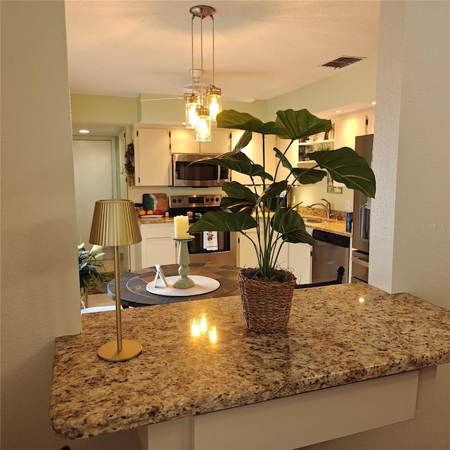 kitchen featuring white cabinetry, appliances with stainless steel finishes, decorative light fixtures, light stone countertops, and kitchen peninsula