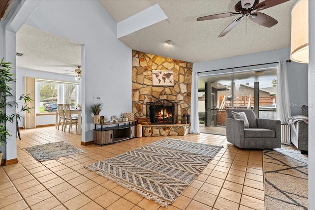 living room with vaulted ceiling, a textured ceiling, light tile patterned floors, ceiling fan, and a fireplace