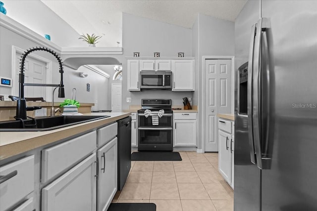 kitchen with appliances with stainless steel finishes, light tile patterned floors, sink, white cabinets, and lofted ceiling