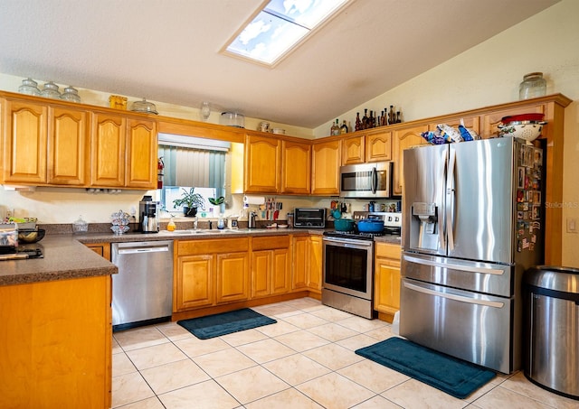 kitchen with stainless steel appliances, light tile patterned floors, lofted ceiling with skylight, and sink