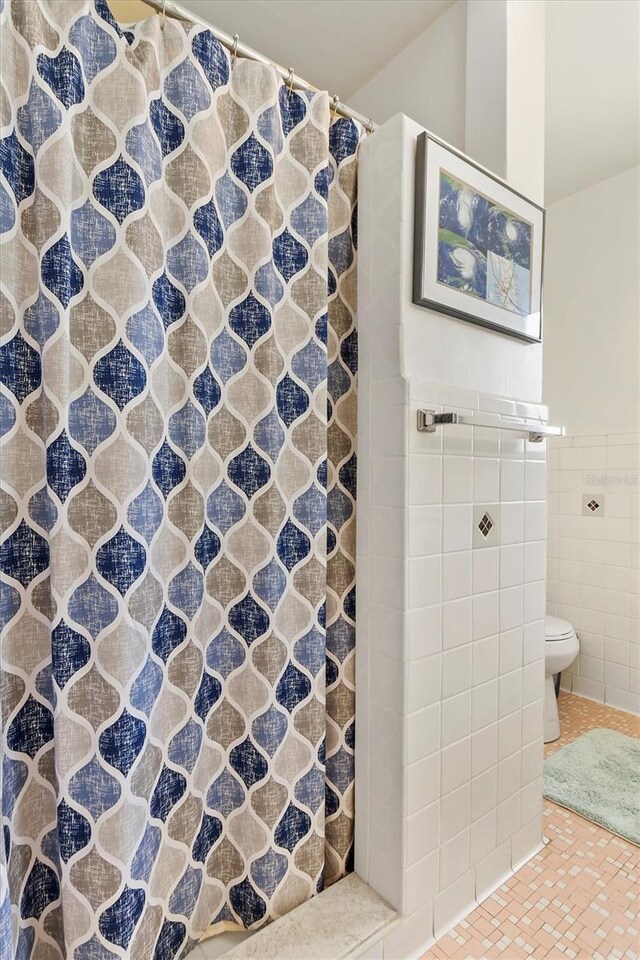 bathroom featuring toilet, tile walls, and curtained shower