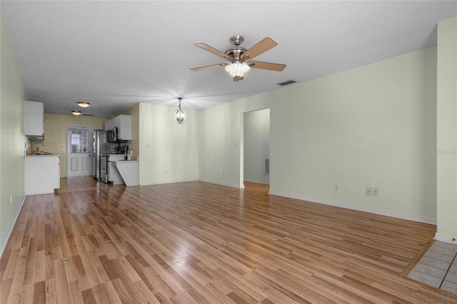 unfurnished living room with ceiling fan with notable chandelier, a textured ceiling, sink, and light wood-type flooring