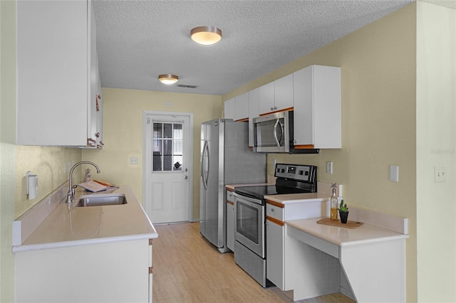 kitchen featuring white cabinetry, appliances with stainless steel finishes, a textured ceiling, sink, and light hardwood / wood-style floors