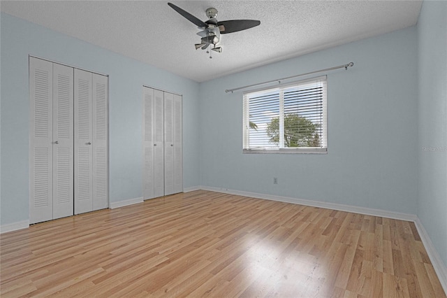 unfurnished bedroom with multiple closets, light hardwood / wood-style floors, a textured ceiling, and ceiling fan