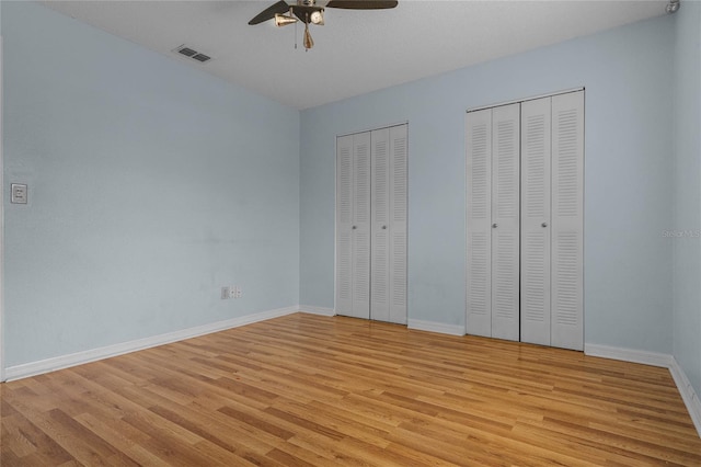 unfurnished bedroom featuring light wood-type flooring, multiple closets, and ceiling fan