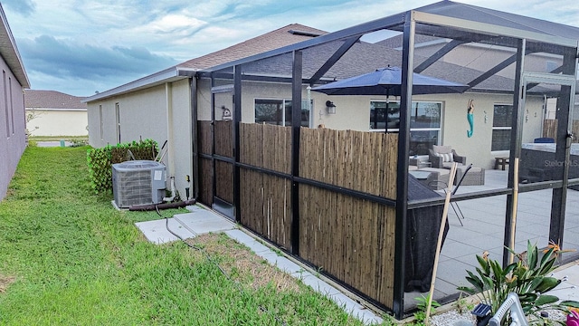 view of home's exterior featuring a lanai, central AC unit, a lawn, and a patio