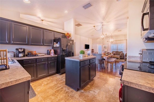 kitchen with black fridge, a textured ceiling, hanging light fixtures, a chandelier, and a center island