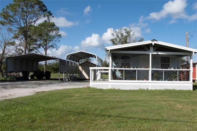 back of property with a carport, a storage unit, a yard, and a sunroom