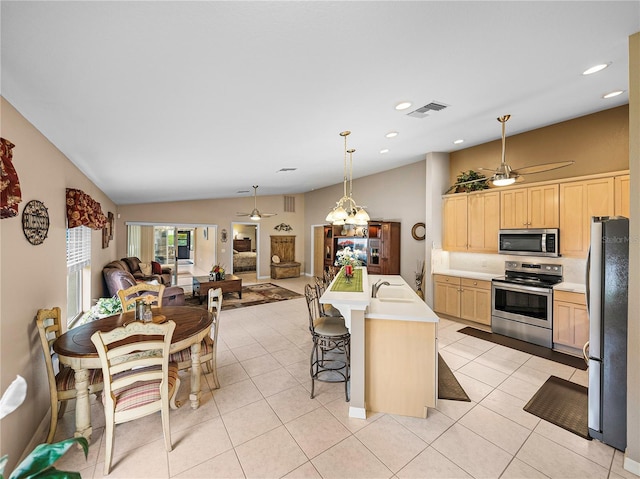 kitchen featuring a kitchen island with sink, light brown cabinetry, lofted ceiling, and appliances with stainless steel finishes