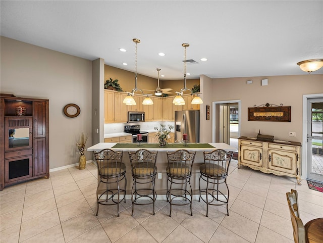 kitchen with light brown cabinetry, hanging light fixtures, light tile patterned floors, a kitchen island, and stainless steel appliances