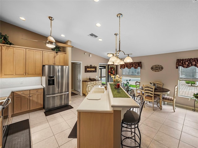 kitchen with vaulted ceiling, decorative light fixtures, light tile patterned floors, stainless steel fridge with ice dispenser, and a center island with sink