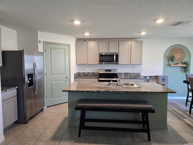 kitchen with a textured ceiling, a kitchen island with sink, and stainless steel appliances