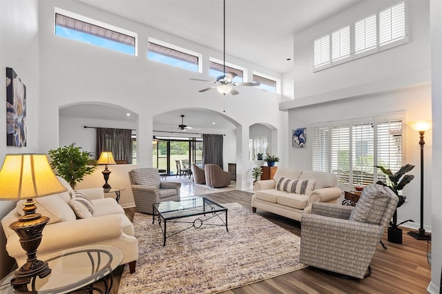 living room with ceiling fan, a towering ceiling, a healthy amount of sunlight, and hardwood / wood-style flooring