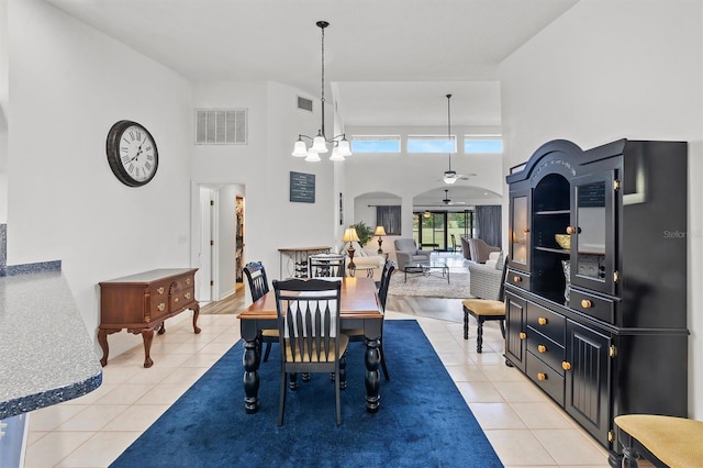 dining room with ceiling fan with notable chandelier, light tile patterned floors, and a high ceiling