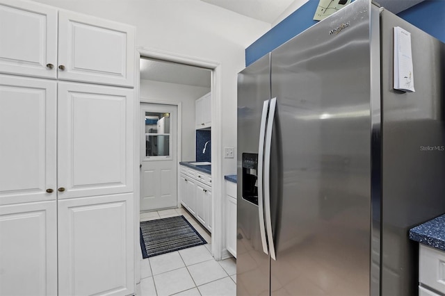 kitchen with white cabinets, light tile patterned flooring, and stainless steel fridge