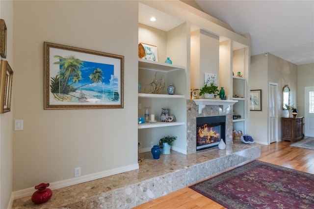 interior space with built in shelves, hardwood / wood-style flooring, vaulted ceiling, and a premium fireplace