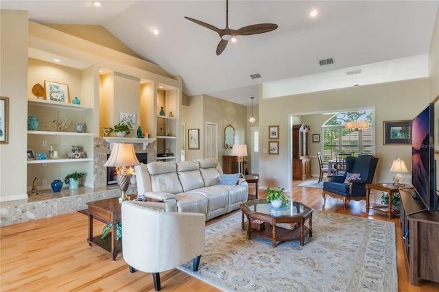 living room featuring built in shelves, light hardwood / wood-style flooring, ceiling fan, and a high end fireplace