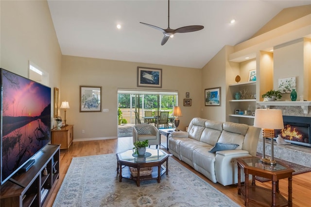 living room with ceiling fan, a high end fireplace, light wood-type flooring, and high vaulted ceiling