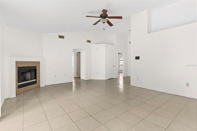 unfurnished living room with high vaulted ceiling, ceiling fan, a tile fireplace, and light tile patterned floors