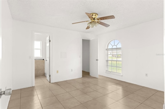 unfurnished room with ceiling fan, a healthy amount of sunlight, light tile patterned floors, and a textured ceiling