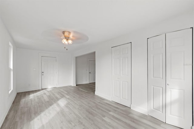 unfurnished bedroom with multiple closets, light hardwood / wood-style floors, and ceiling fan